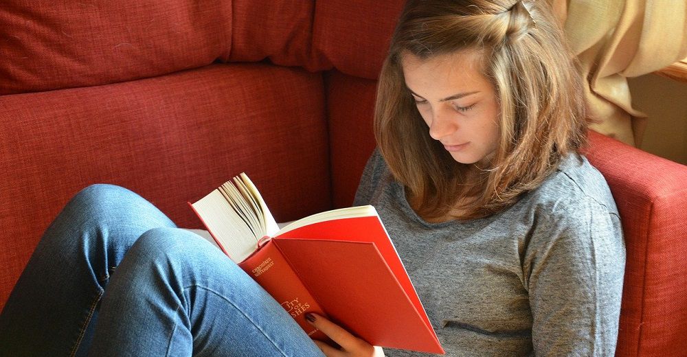 Девочка-подросток читает книгу на диване